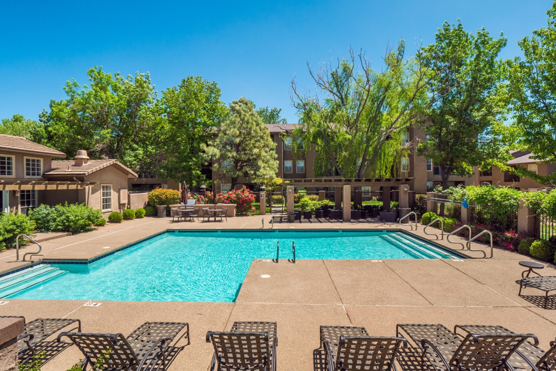 Outdoor pool and patio with lounge chairs in the foreground and apartment complex in the background